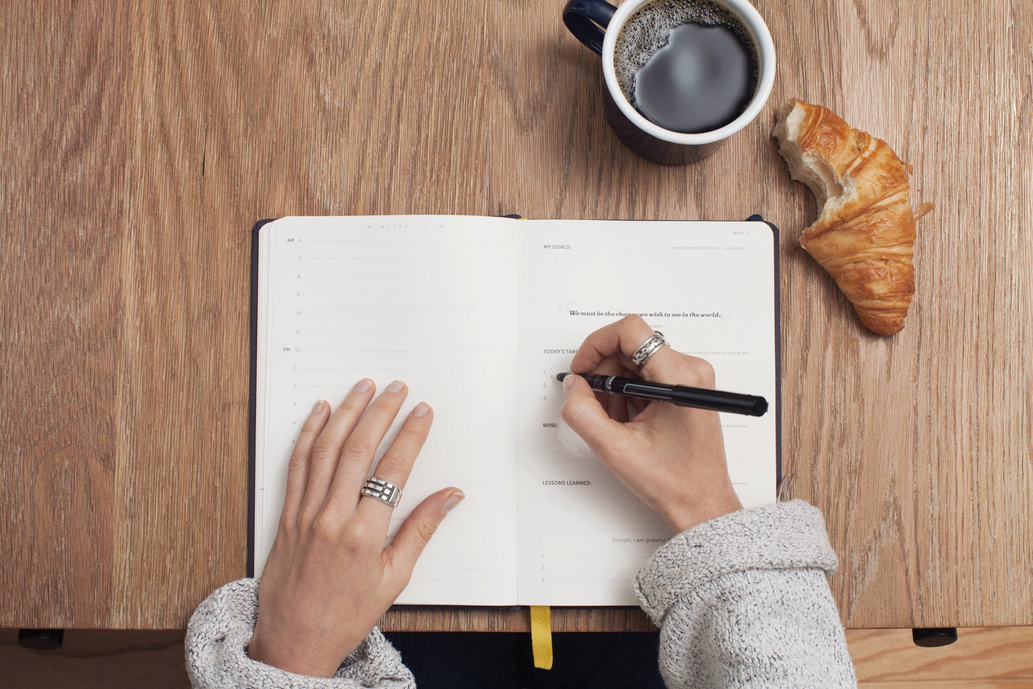 someone taking notes in a notebook with coffee and croissant on tabel