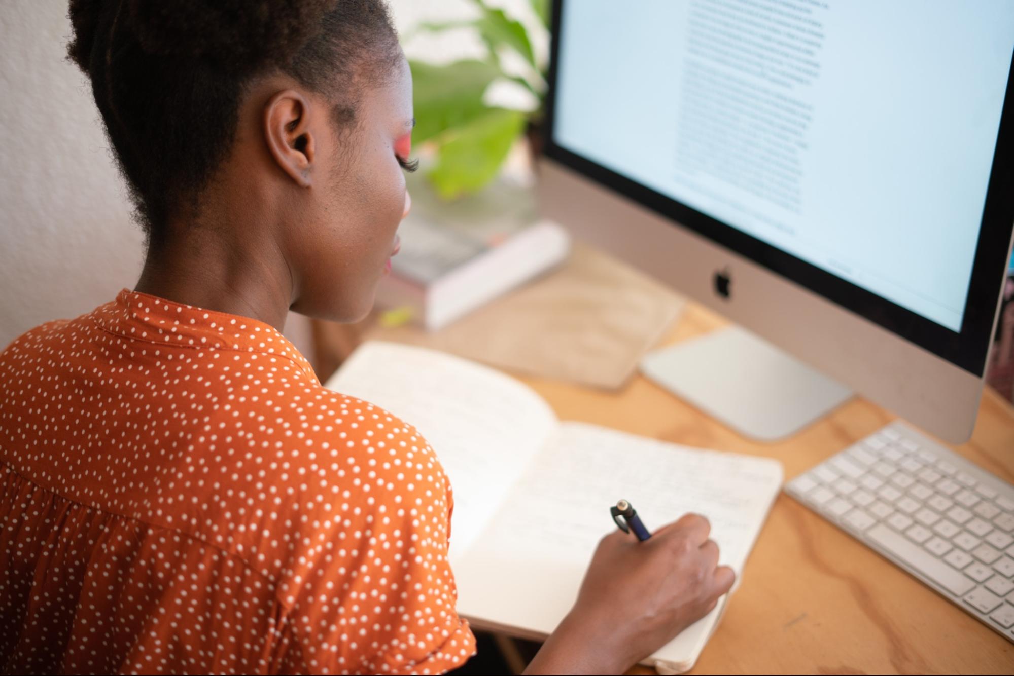 a woman take notes in a notebook at desk with computer