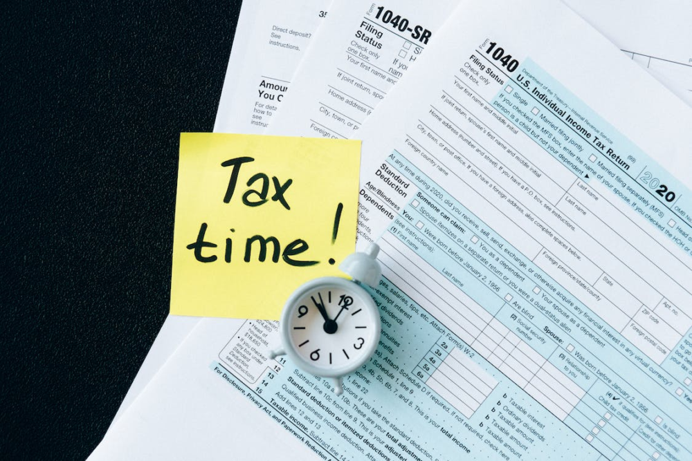 tax forms with miniature clock and sticky note that reads tax time